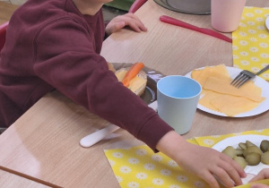 Dzieci siedzą przy stole i zjadają samodzielnie przygotowane śniadanie.