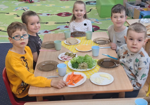 Dzieci siedzą przy stole i zjadają samodzielnie przygotowane śniadanie.