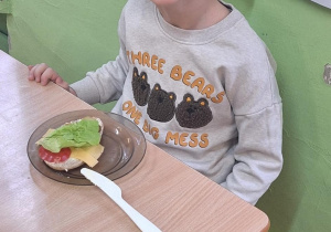 Dzieci siedzą przy stole i zjadają samodzielnie przygotowane śniadanie.