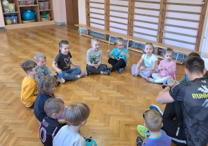 Dzieci siedzą w kole i słuchają pana.