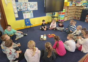 dzieci siedzą w kole na dywanie, na środku leżą produkty do przygotowania posiłku