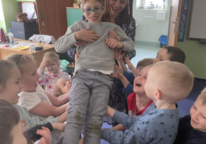 Dzieci wraz z nauczycielem podrzucają chłopca.