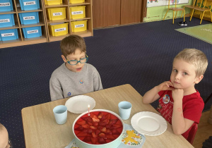 Dzieci siedzą przy stołach, a przed chłopcem stoi ciasto ze świeczką.