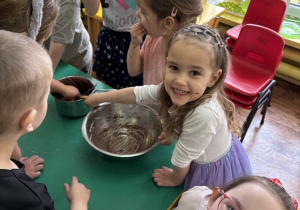 Dzieci zgromadzone przy stole smakują czekoladę.