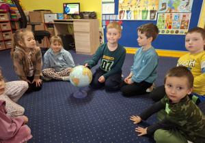 dzieci siedzą w kole oglądają globus