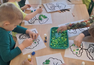 Dzieci przy stoliku wykonują prace plastyczną.