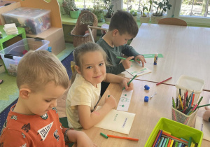 Dzieci przy stoliku wykonują prace plastyczną.
