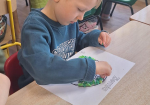 Dzieci przy stoliku wykonują prace plastyczną.