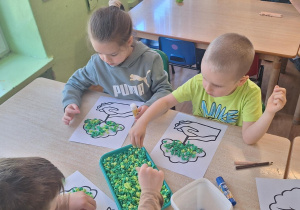 Dzieci przy stoliku wykonują prace plastyczną.