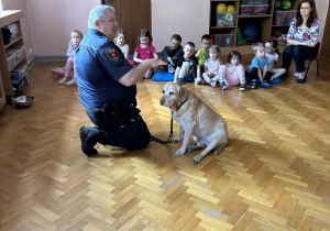 Dzieci siedzą i słuchają pana policjanta.