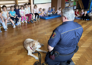 Dzieci siedzą i słuchają pana policjanta.