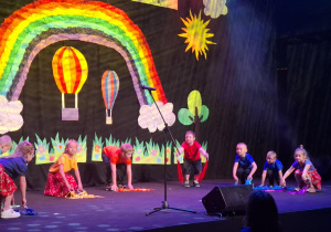 dzieci w kolorowych strojach występują na festiwalu na tle tęczy, prezentują piosenkę