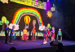 dzieci w kolorowych strojach występują na festiwalu na tle tęczy, prezentują piosenkę