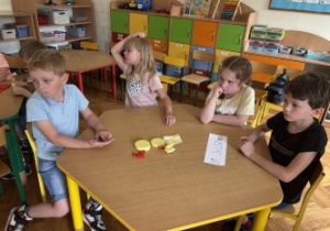 Dzieci siedzą przy stole i rozwiązują zadania matematyczne.