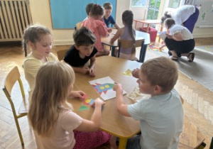 Dzieci siedzą przy stole i rozwiązują zadania matematyczne.