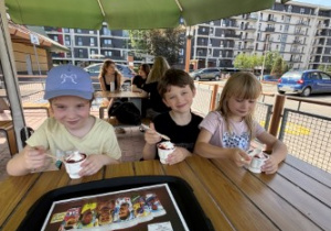 Dzieci siedzą przy stole i zjadają lody.