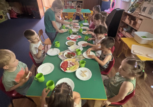 Dzieci siedzą przy stole i jedzą śniadanie.
