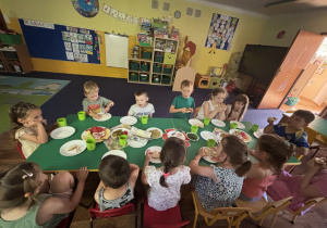 Dzieci siedzą przy stole i jedzą śniadanie.