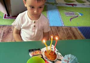 Chłopiec siedzi przy stole na którym stoi ciastko ze świeczkami.