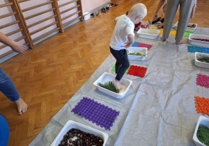dzieci biorą udział w zajęciach sensorycznych, dotykają, chodzą, obserwują materiały przyrodnicze