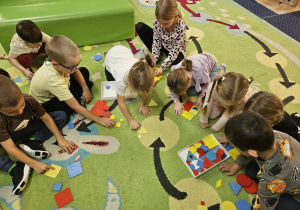 Dzieci siedzą na podłodze i bawią się klockami dienesa.