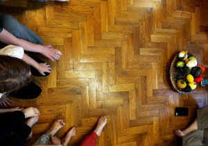 Dzieci siedzą na podłodze i bawią się dyniami przy muzyce.