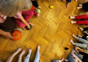 Dzieci siedzą na podłodze i bawią się dyniami przy muzyce.