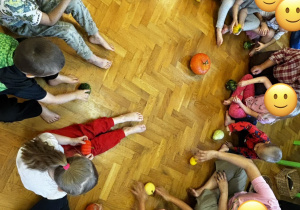 Dzieci siedzą na podłodze i bawią się dyniami przy muzyce.