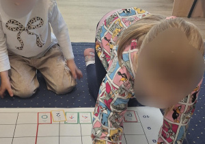 Dzieci siedzą na dywanie wokół maty do kodowania.