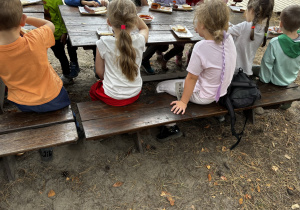 Dzieci jedzą pieczone kiełbaski z ogniska.
