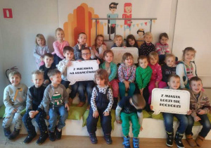 Dzieci z grupy 2 i 4 siedzą na podeście i trzymają hasła związane z Łodzią.