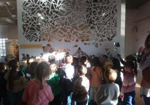 Dzieci z grupy 2 i 4 oglądają błyszczącą mozaikę na ścianie.
