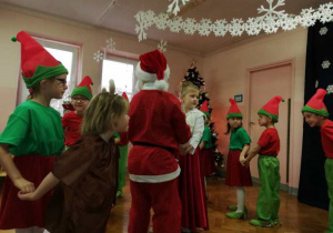 Święty Mikołaj wraz z żoną, elfami i reniferami tańczą.