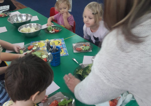 Nauczyciel rozkłada warzywa do degustacji na talerzyki dzieci.