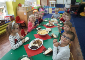 Dzieci siedzą przy stołach i zjadają słodkości.