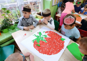 Dzieci wykonują wydzierankę z kolorowego papieru.