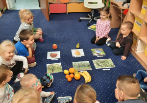 Dzieci siedzą w kole i poznają owoce.