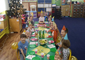 Wszystkie dzieci siedzą przy kolorowym stole.