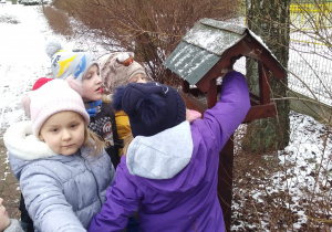 Dzieci wsypują ziarenka do karmnika.