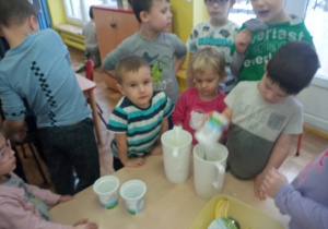 Dzieci stoją przy stoliku i wykonują bananowy koktajl