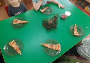 Dzieci siedzą przy stole. Na talerzykach leżą kawałki pizzy.