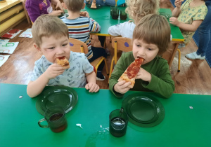Dzieci siedzą przy stole. Na talerzykach leżą kawałki pizzy.