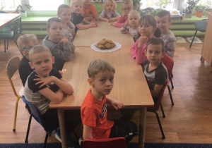 Dzieci siedzą przy stole, a na stole stoi talerz z ciasteczkami owsianymi.