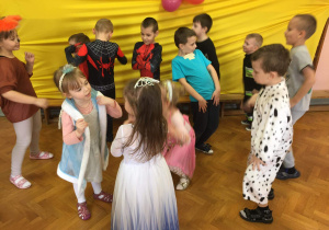 Grupa dzieci w przebraniach tańczy na tle żółtej dekoracji.