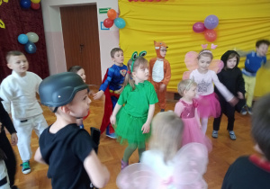 Grupa dzieci w przebraniach karnawałowych tańczy na sali gimnastycznej.