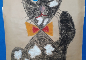 Praca plastyczna wykonana przez dzieci. Na papierze pakowym dużego formatu narysowany czarny kot w baiałe łaty.
