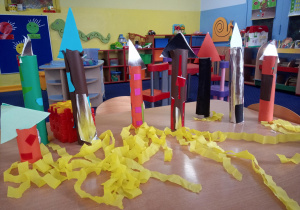 prace plastyczne wykonane przez dzieci- na stole stoją kolorowe rakiety z rolek po ręcznikach papierowych.