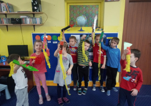 Grupa dzieci stoi przy niebieskiej tablicy. dzieci trzymają papierowe, kolorowe rakiety.