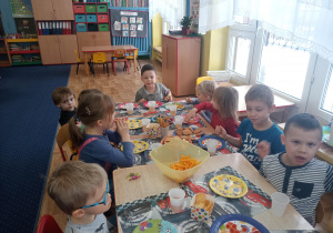 Przy złączonych stołach, na których ustawione są talerze z przysmakami, siedzą dzieci.