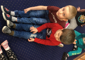 Dwóch chłopców siedzi na podłodze i porównuje długość swoich nóg.